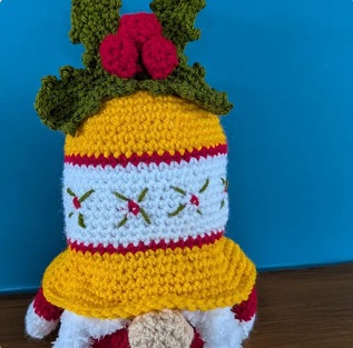 Belle, a gold and cream crocheted bell gonk with embroidered detail and holly on top