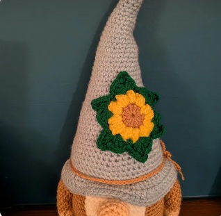 Daisy, a crocheted gonk with a tall stone-coloured hat and a large crocheted sunflower on the front