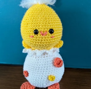 Doris, a yellow crocheted chick sitting in a white spotted eggshell