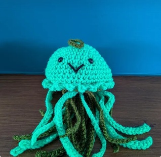 Nessa, a turquoise crocheted jellyfish with a stitched smile and eight curling tentacles