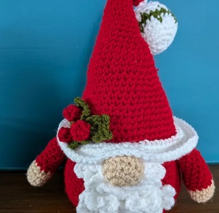 Nicholas, a crocheted Santa gonk with a tall red hat, white beard and crocheted holly on the brim