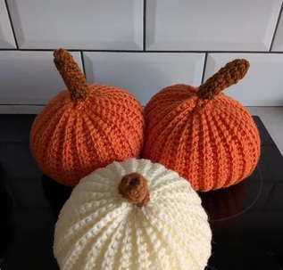 Three crocheted pumpkins, two orange and one cream, each with a twisted stalk