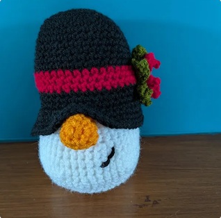Wilf, a crocheted snowman gonk in a black top hat with a red band and a sprig of holly