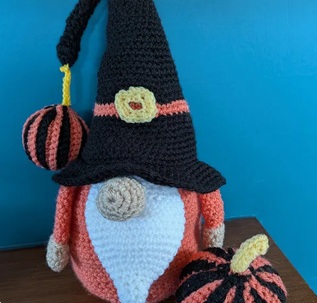 Wilhelmina, a crocheted Halloween gonk in a tall black witch hat with a striped pumpkin hanging from the tip